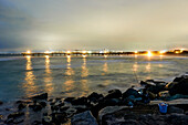 Abendaufnahme mit Blick von The Spit über das Wasser und am Steg vorbei auf die beleuchtete Stadt Surfers Paradise