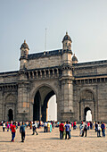 People in front of the Gateway of India monument built to commemorate the landing of King George V completed in 1924. The stone arch is built in South Mumbai on the shoreline of the Arabian Sea.