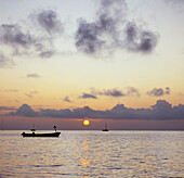 Silhouett von Booten, die auf ruhigem Meer verankert sind, und Sonne, die bei Sonnenuntergang unter Wolken scheint