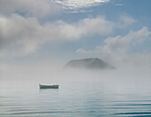 Small boat floating on rippling blue water and sea mist rolling in with Mount Maunganui peaking through in the Background