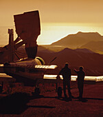 Two men standing beside aeroplane being filled with fertiliser at sunrise