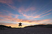 Looking up from the beach at lone lifeguard tower at sunset