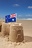 Australian flag on top of group of three sandcastles at the beach