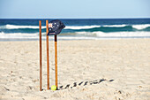 Kappe mit australischer Flagge, die auf hölzernen Kricketstümpfen und Tennisball am Strand ruht