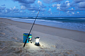 Fishing rod, bucket and lamp on the sand near the sea - early evening