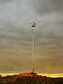 Hohe Flutlichter, die am Hafen von Tauranga auf den Export-Stapel mit stürmischem Himmel am frühen Abend scheinen