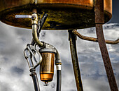 Old farm gasoline pump against stormy sky