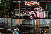 Car Wrecker Yard and pink building with car wreck perched on upstairs balcony