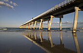 Reflections in the wet sand of long jetty stretching out to sea