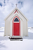Old wooden church with red door amongst snowy landscape