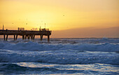 People walking and fishing on ocean pier as the sun set over the ocean