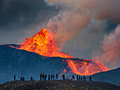 Wanderer erfreuen sich am Feuerwerk vom Observation Hill, während glühende Lava aus dem Vulkan Fagradalsfjall in Island ausgestoßen wird