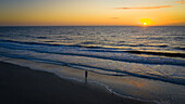 Frau fotografiert den Sonnenaufgang am Strand.