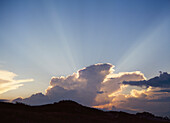 Sunrays shining up from clouds into blue sky as sunset
