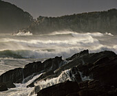 Large waves rolling into shore and crashing over rocky coastline