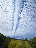 Jetstream dissipating path through fluffy clouds over rural farmland