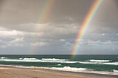 Double rainbow against grey clouds the the beach