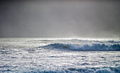 Wellen kräuseln sich und brechen während des Zyklons Ola mit stürmischem Himmel