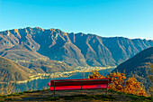 Bank mit Panoramablick über den Luganersee und das Dorf mit dem Berg Generoso an einem sonnigen Tag in Vico Morcote, Tessin in der Schweiz