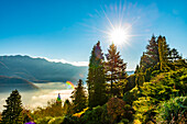 Mountain View over Trees and Lake Lugano with Cloudscape with Sunbeam on Clear Sky in Lugano, Ticino in Switzerland.