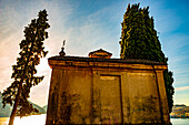 Kirche mit Zypresse und Luganersee mit Berg und blauem Himmel im Park San Michele in Castagnola in Lugano, Tessin in der Schweiz