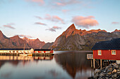 Fishing boats, red houses in Hamnoy harbour, Moskenesoy, Lofoten, Norway. Sunlight on mountain peaks.
