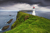 Blick auf Steilküste und  Mykines Holmur Leuchtturm bis Mykines, Färöer Inseln. Dunkle Wolken.