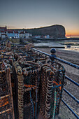 Evening view of small port town of Staithes, Yorkshire, England, UK. In the foreground lobster cages on railings.