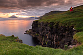 Small red lighthouse on a green cliff. mountain in the sea. Velbastadur, Streymoy, Faroe Islands.