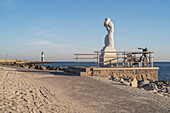 View of the western pier with the lighthouse in Warnemünde and the statue in the foreground in the morning.