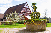 Easter fountain decorated with colorful Easter eggs in the churchyard of St. Nikolaus in Pinzberg in Franconian Switzerland, Bavaria, Germany