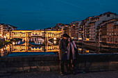 Paar schaut auf Handy auf der Brücke Santa Trinita, Abendstimmung über der Brücke Ponte Vecchio, Brücke über Arno, Florenz, Toskana, Italien, Europa