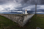 Leuchtturm Loop Head. Dunkle Regenwolken. Mauer im Vordergrund. Kilbaha South, Kilballyowen, County Clare, Irland.