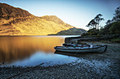 2 rowing boats are on the shore of the lake. Old stone jetty. mountains in the background. Sunrise. Doo Lough, Clashcame, Kilgeever, County Mayo, Ireland.