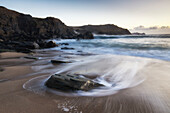 Ziehende Wasserspuren an Felsen am Sandstrand. Clogher Strand, Dunurlin, County Kerry, Irland.