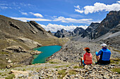 Mann und Frau beim Wandern machen Pause und blicken auf Lago Vallonasso, Chambeyron-Gruppe, Val Maira, Cottische Alpen, Piemont, Italien