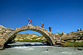 Drei Wanderer gehen auf Steinbrücke über Bergbach Reculaz, Nationalpark Vanoise, Vanoise, Savoyen, Frankreich