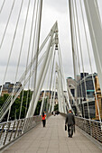 People walking across Jubilee Footbridge next to Cannon St Railway Bridge, London