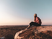Eine Frau sitzt auf einem Felsen und beobachtet von einem Aussichtspunkt aus den Sonnenaufgang