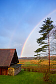 Rural scene, a rainbow in the sky over a barn, after rain.