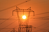 Strommast und Stromleitungen mit Sonne dahinter.