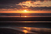 Paar umarmt am Cannon Beach mit dramatisch bewölktem Himmel bei Sonnenuntergang, USA