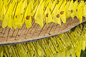 Yellow prayer flags stuck in sand over reflecting water at a wat temple, Thailand