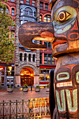 Totem pole on street with historic apartment building behind, Seattle, USA