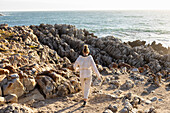 Teenage girl on a beach, exploring the jagged rocks at sunset, De Kelders, Western Cape, South Africa.