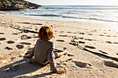 Kleiner Junge sitzt an einem Sandstrand