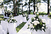 A garden with tables laid under the shade of tall trees, set for a wedding