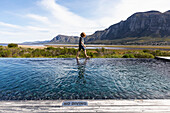 Eight year old boy walking around the edge of an infinity pool, a mountain backdrop, Klein Mountains,South Africa