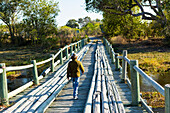 Ein Junge, der allein über eine Holzbrücke über Marschland geht