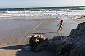 A boy running n the sand at the water's edge on a sandy beach, Grotto Beach, South Africa